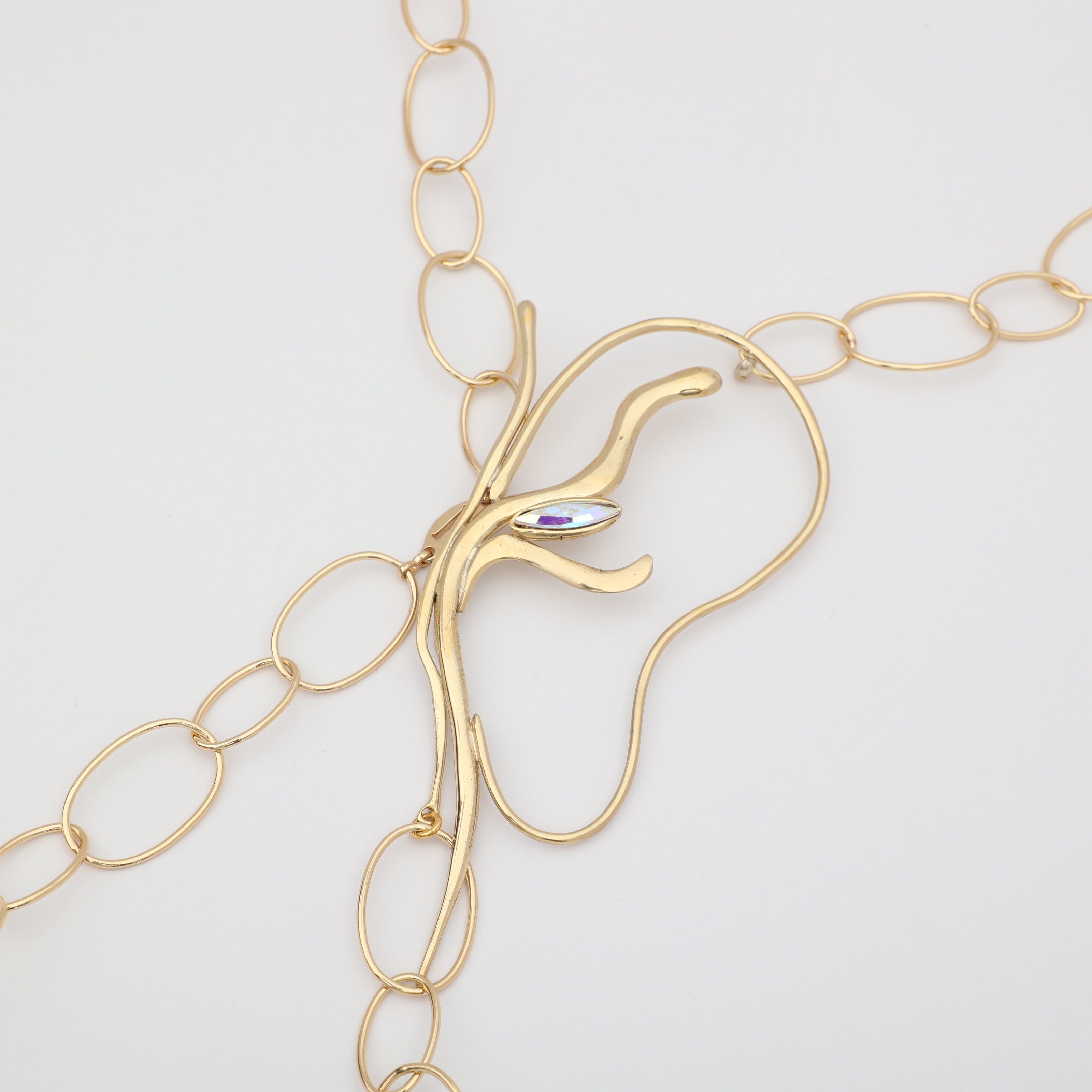 Flat lay close-up of handmade brass abstract pendant with iridescent marquise crystal and oval link chain, unique Greek designer jewelry.
