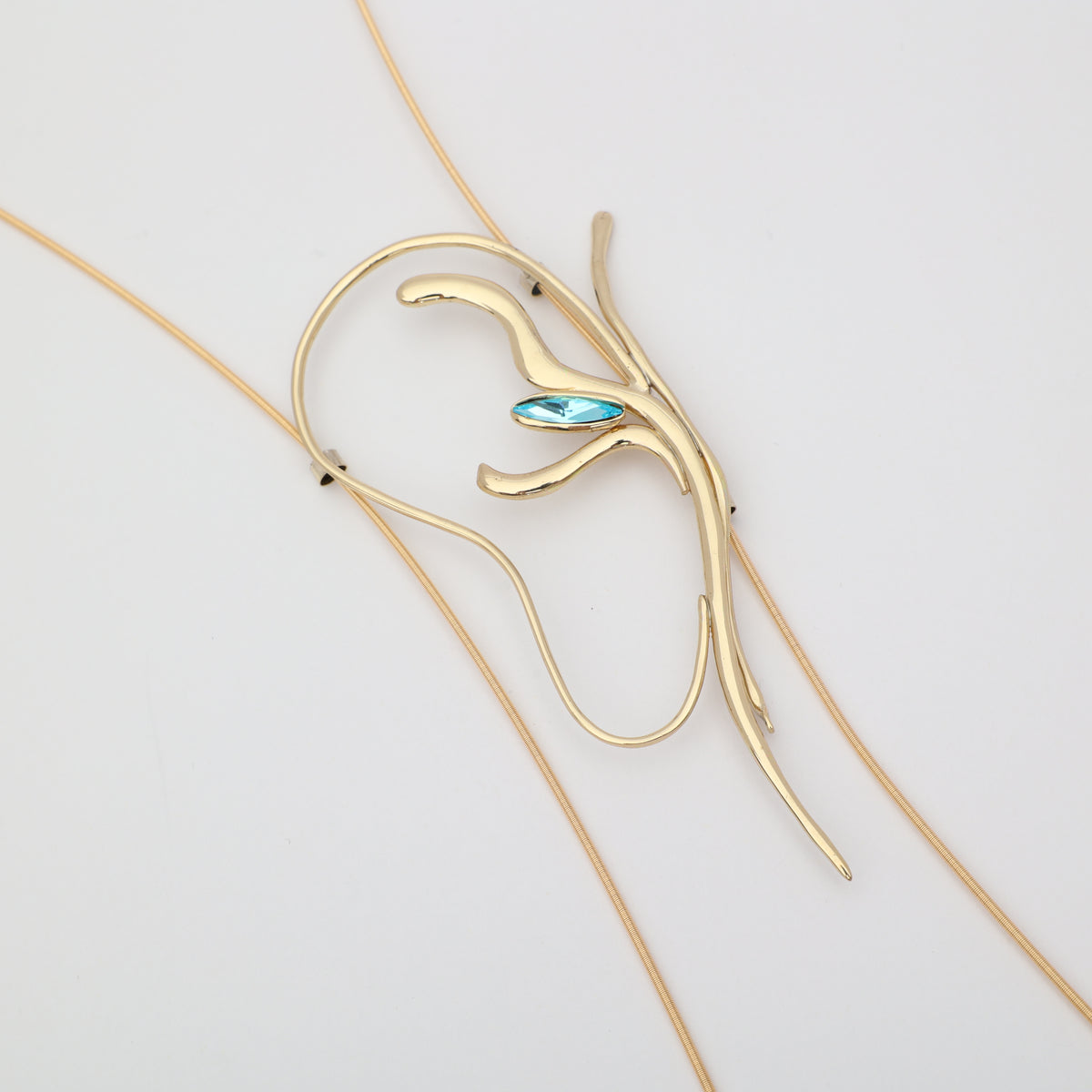 Flat lay of handmade brass abstract lariat necklace with aqua blue crystal, unique Greek designer jewelry.