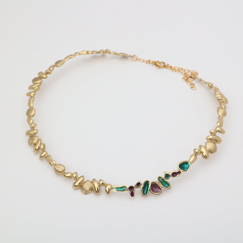 Gold necklace with embedded gemstones on a light gray background