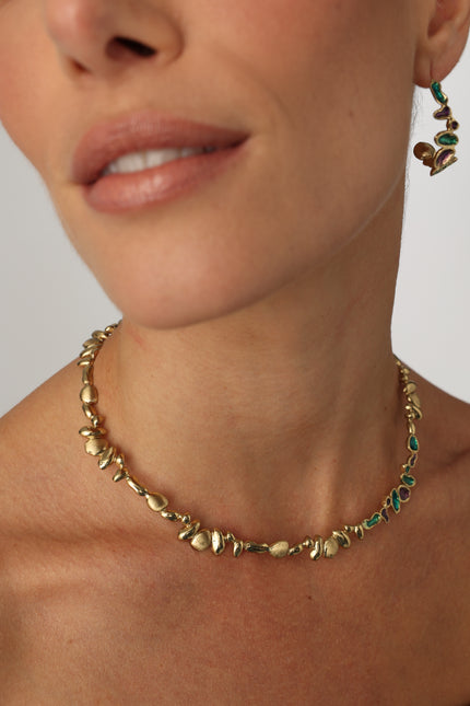 Close-up of a person wearing a gold bracelet with green stones on a neutral background