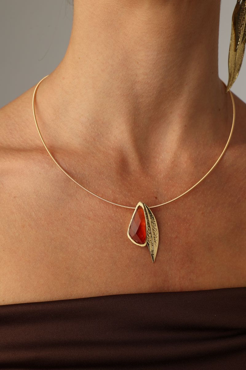 Handmade brass wire collar necklace with sculptural stone and leaf motif, close-up on neck
