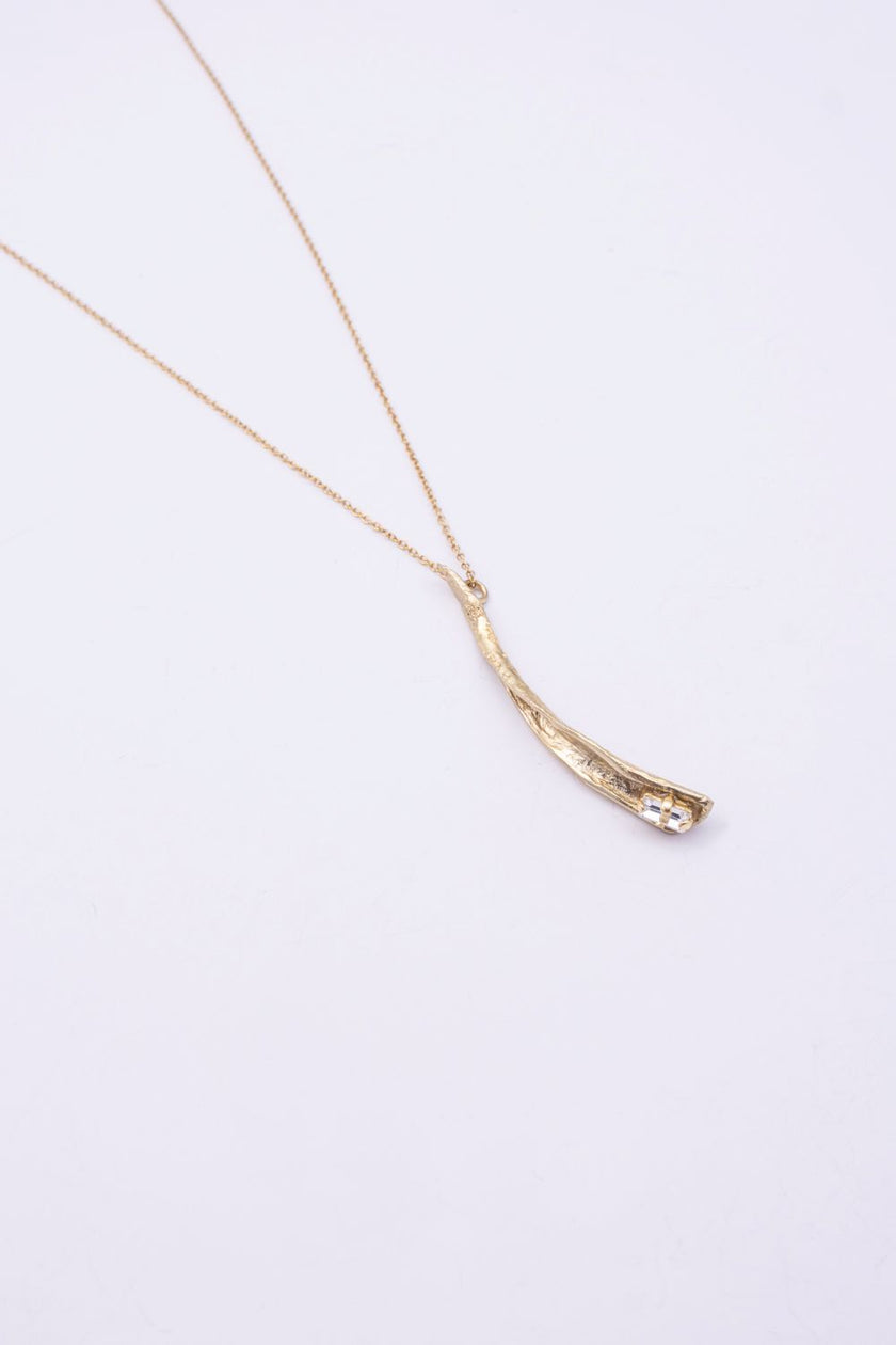 Glade handmade gold-plated brass pendant necklace with curved leaf-like pendant and clear baguette-cut crystal on a white background
