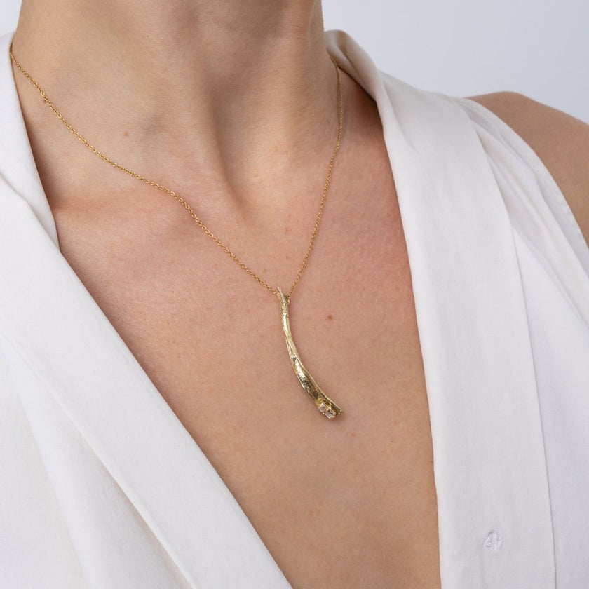 Woman wearing the Glade gold-plated pendant necklace with a textured leaf-shaped drop and baguette crystal on a fine gold chain, Savage Flora