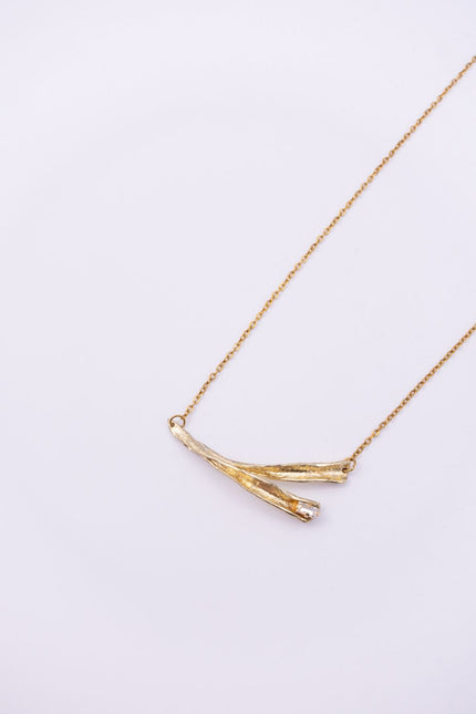 Pixie handmade gold-plated brass pendant necklace with crossed textured leaves and clear baguette-cut crystal on a white background