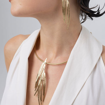 Woman wearing the Pine gold-plated choker necklace with a long pendant of layered pine-needle blades and matching earrings, Savage Flora