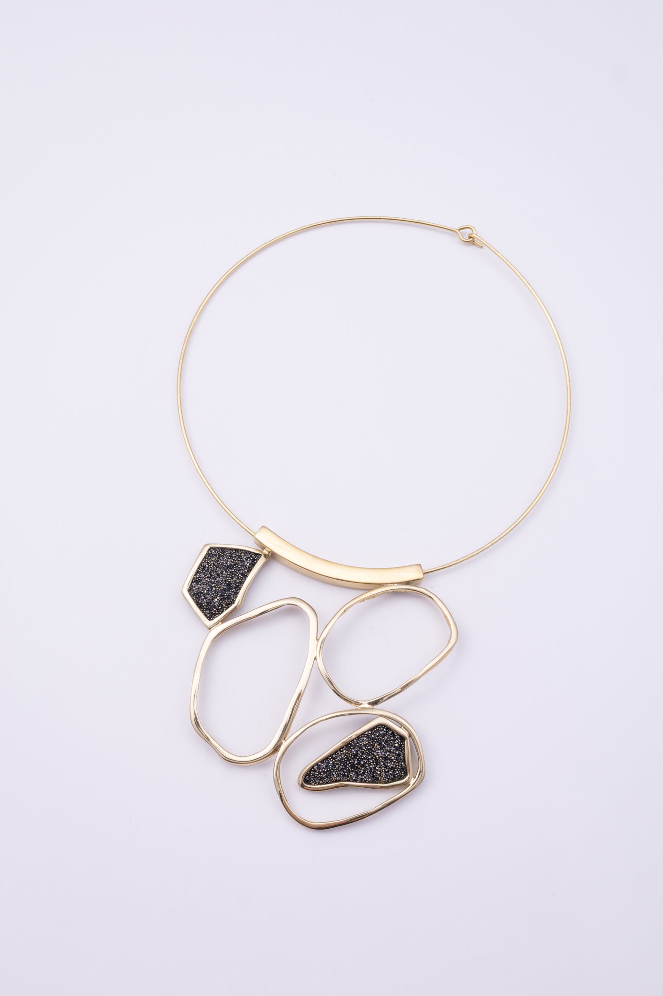 Glow Necklace angle view: handmade brass sculptural necklace with curved brass bar and cascading loops