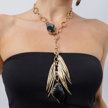 Woman wearing the Kite gold-plated chain necklace with black resin stones and long pendant of sculpted gold blades, Savage Flora