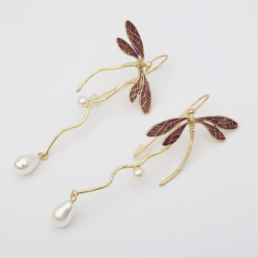 Dragonfly-shaped earrings with pearl accents on a light background