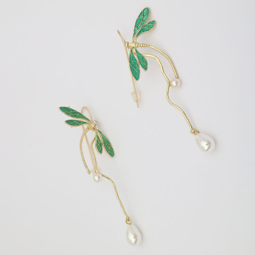 Gold earrings with green leaves and pearl drops on a light gray background