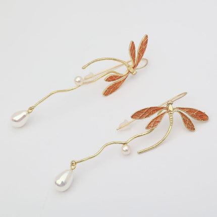 Pair of gold butterfly earrings with pearl drops on a light gray background