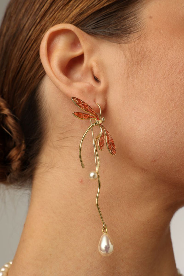 Buzz Earrings — handmade brass dragonfly drop earrings with orange enamel wings and freshwater pearl drops, worn on model