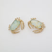 Pair of crab-shaped earrings with gold detailing on a light gray background