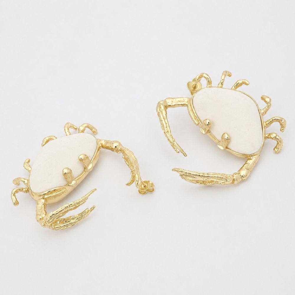 Pair of crab-shaped earrings with gold and white details on a light gray background