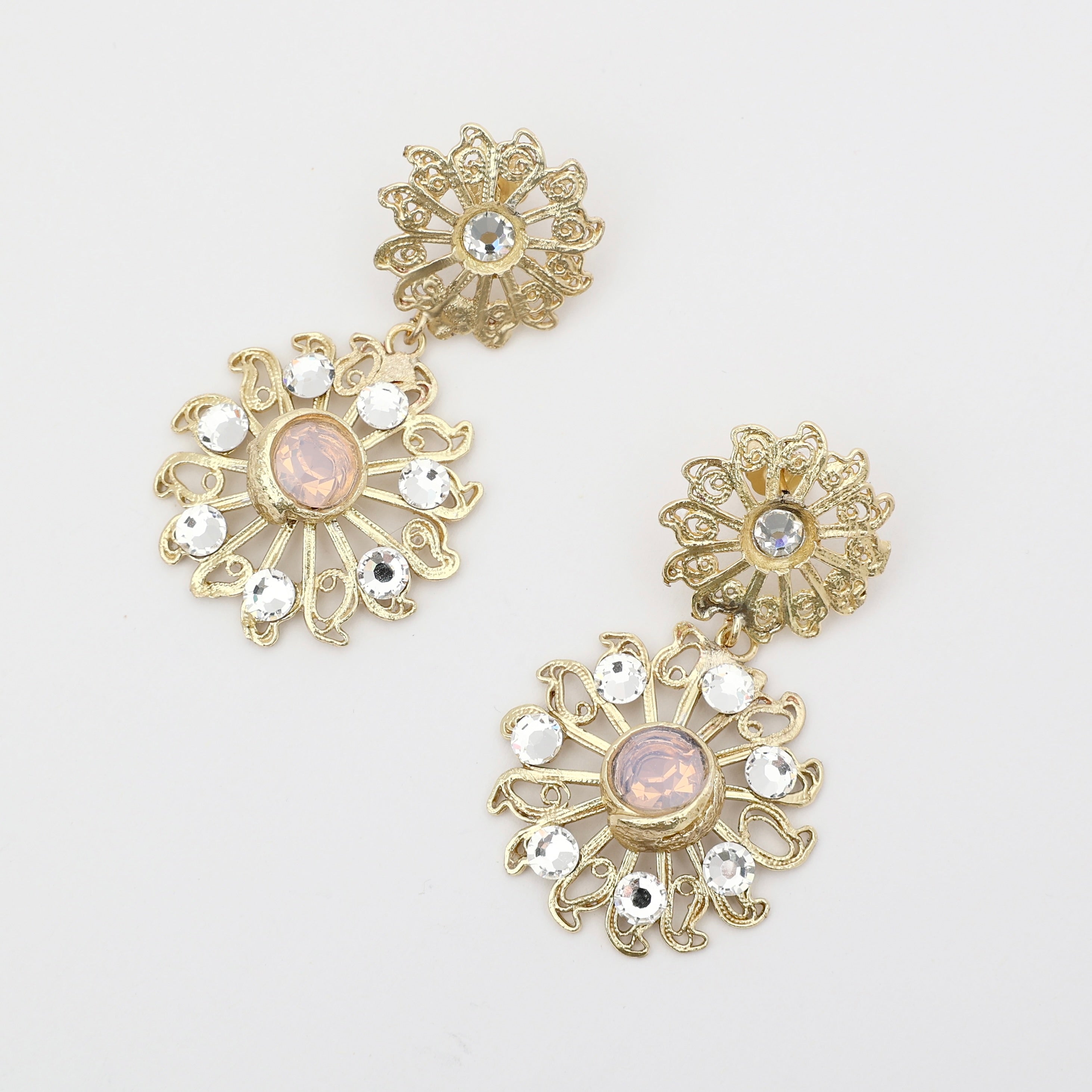 Close-up of handmade artisan brass earrings with blush pink crystals.