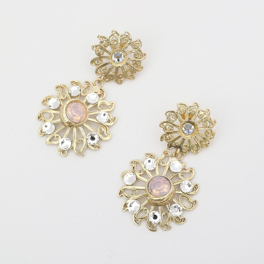 Close-up of handmade artisan brass earrings with blush pink crystals.