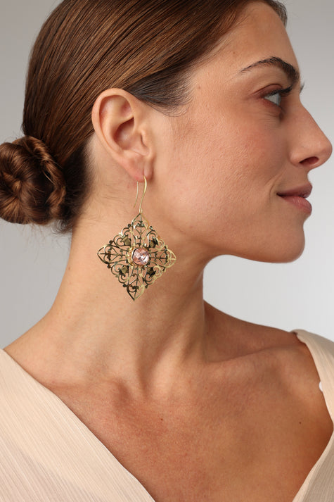 Woman wearing a decorative earring with a pink gemstone on a neutral background