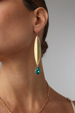 Gold earring with a green gemstone worn by a person on a plain background