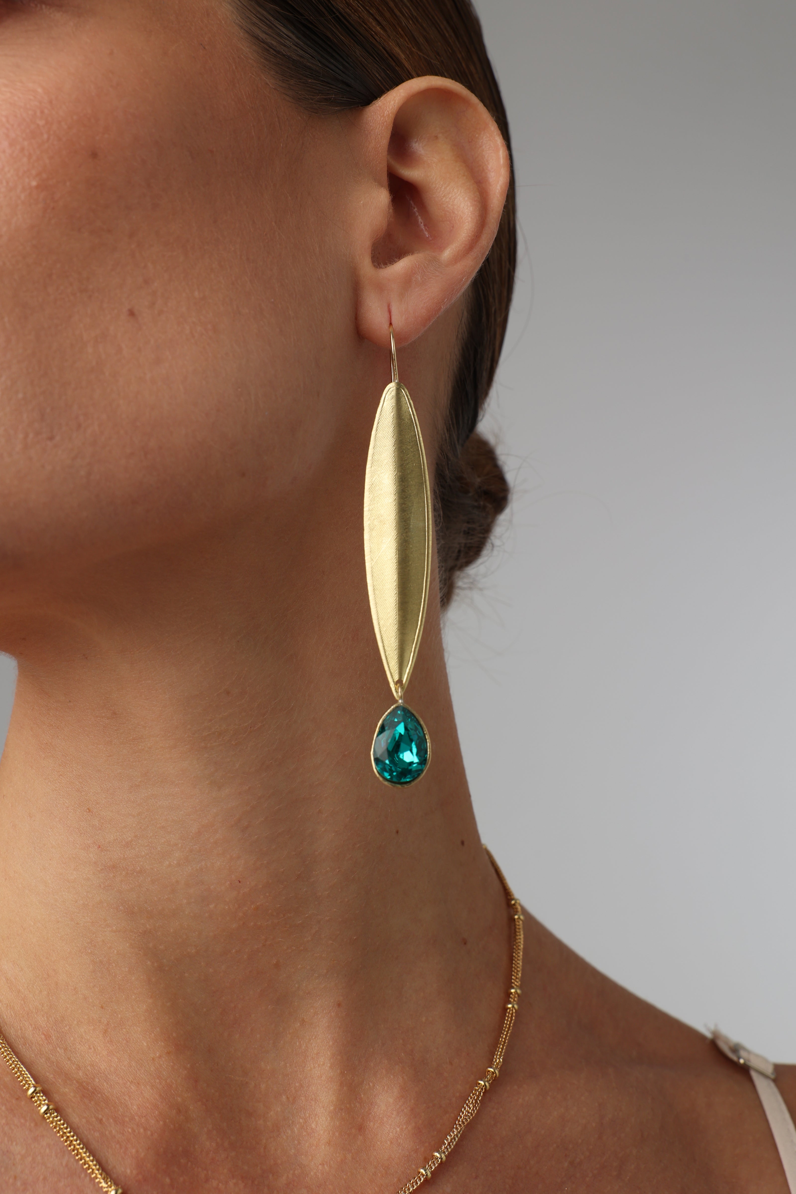 Gold earring with a green gemstone worn by a person on a plain background