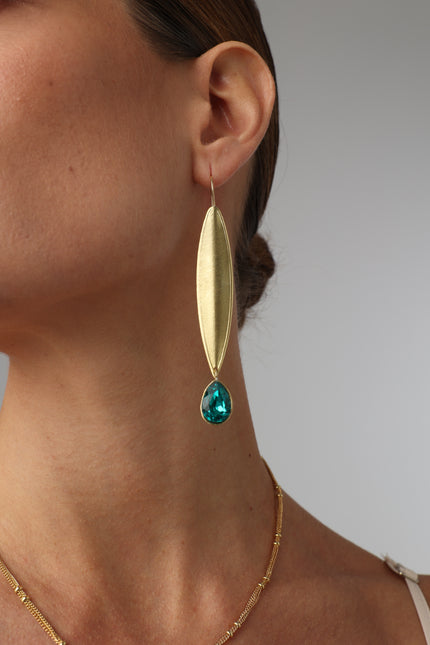 Gold earring with a green gemstone worn by a person on a plain background