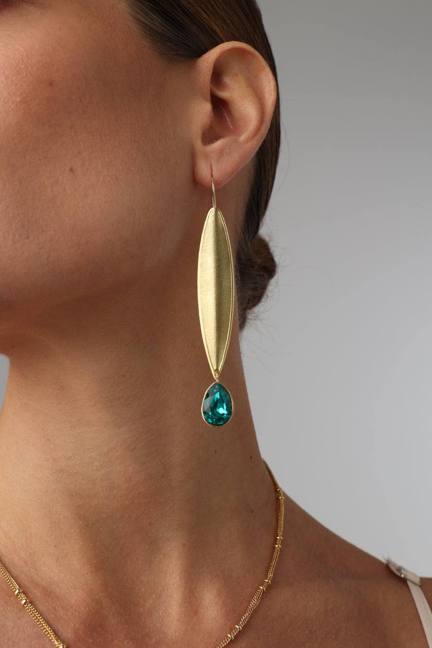 Gold earring with a green gemstone worn by a person on a plain background