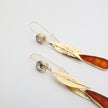 Pair of handmade bronze leaf drop earrings with amber/rust crystals on a white background.