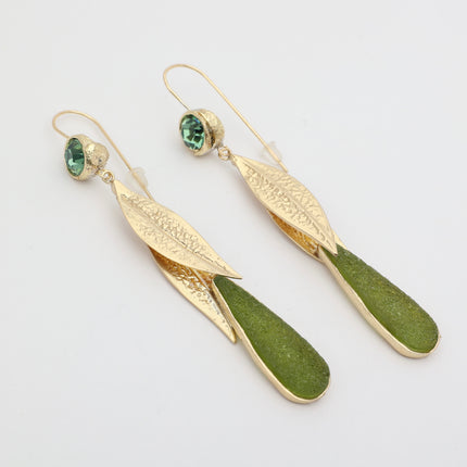 Pair of handmade bronze leaf drop earrings with green crystals on a white background.
