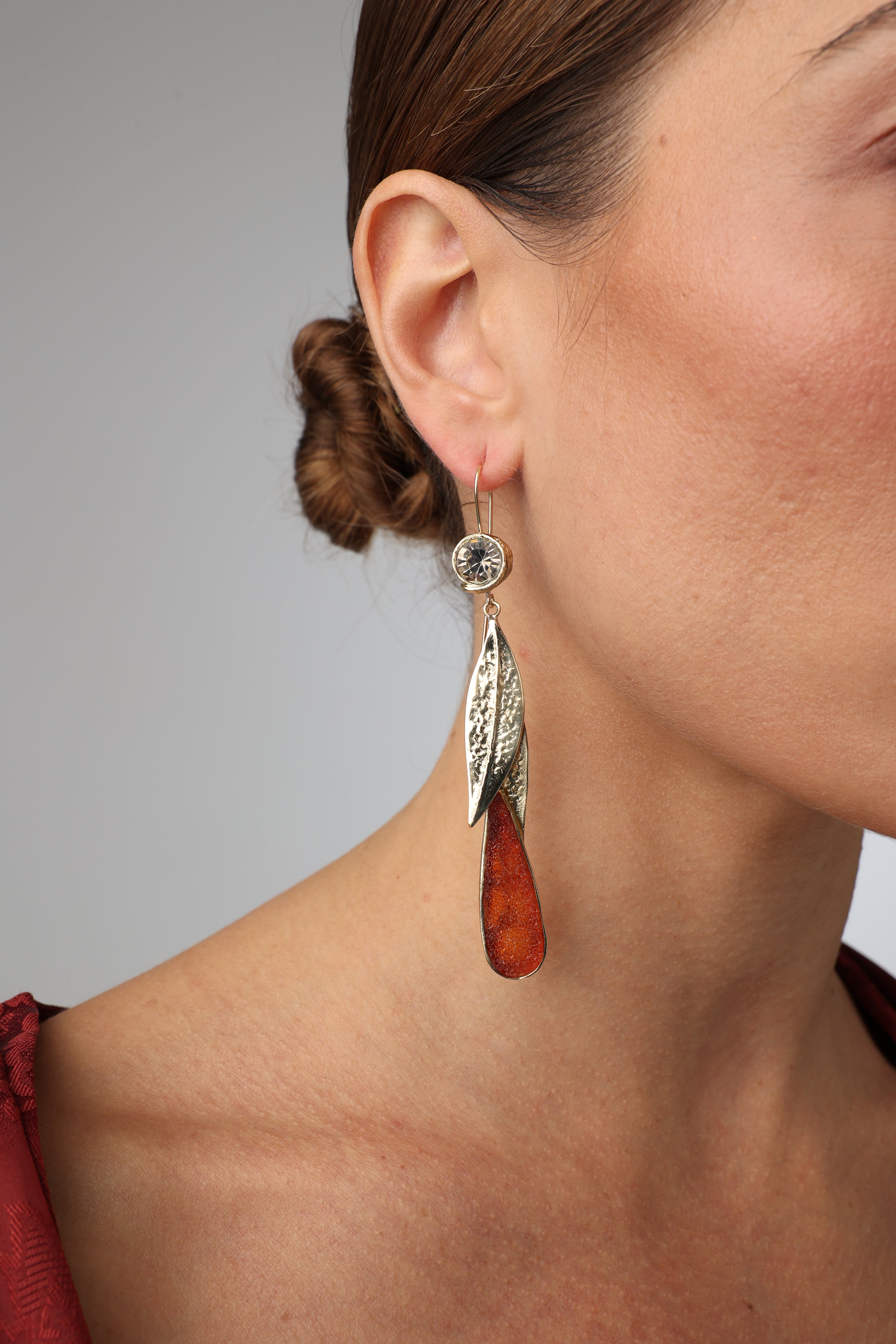 Woman wearing long bronze leaf drop earrings with amber crystals.