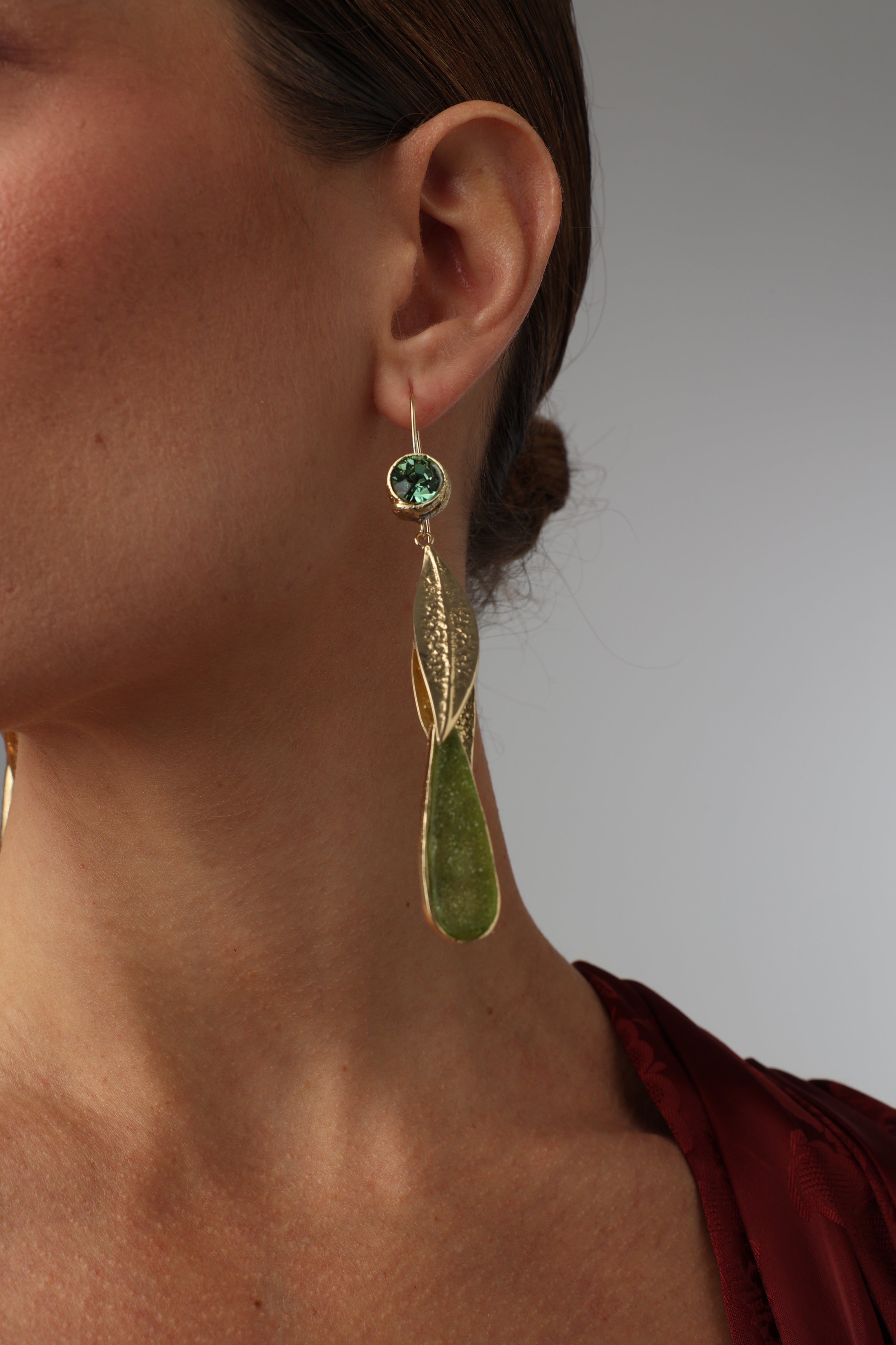 Woman wearing long bronze leaf drop earrings with green crystals.