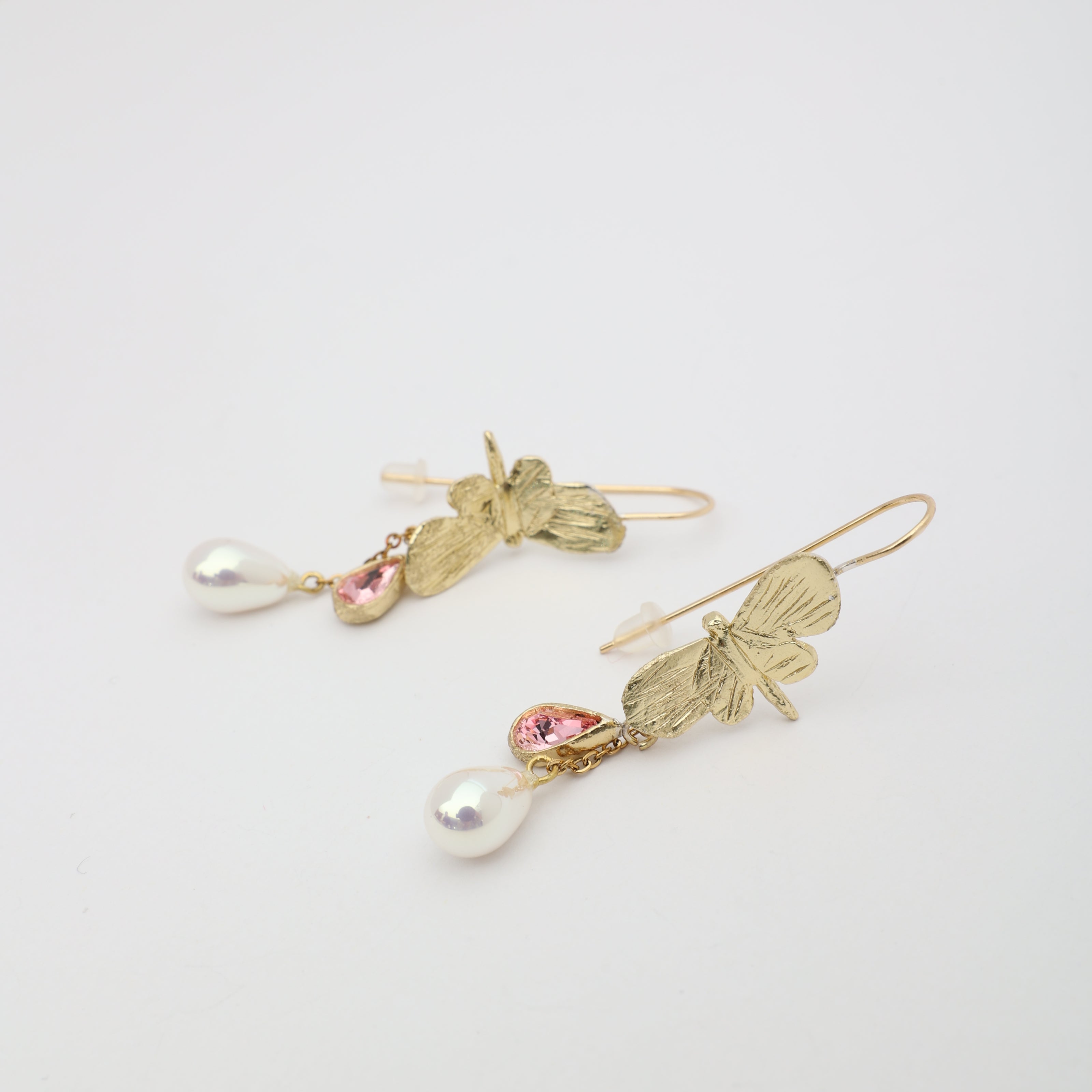 Pair of handmade bronze butterfly earrings with pink crystals and pearls on a white background.