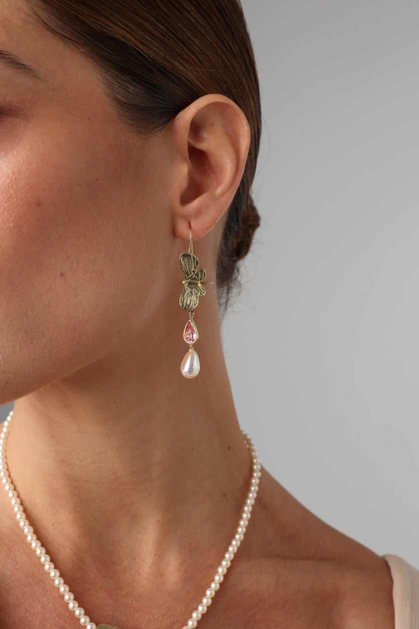 Close-up of a woman wearing bronze butterfly earrings with crystals and pearls.