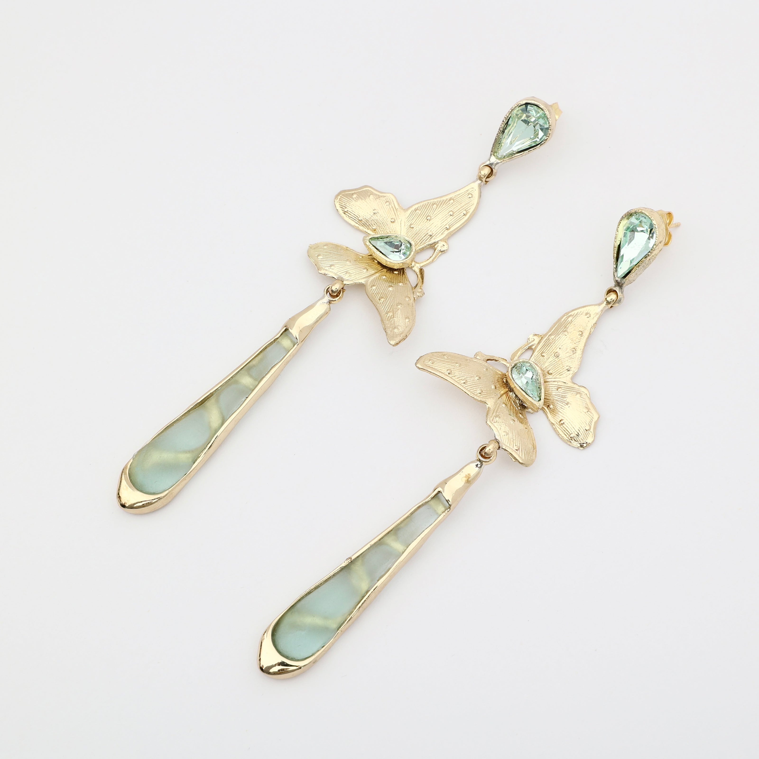 Pair of handmade bronze butterfly earrings with green crystals and long green drops on a white background.