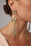 Close-up of a woman wearing bronze butterfly earrings with green crystals and long green drops.