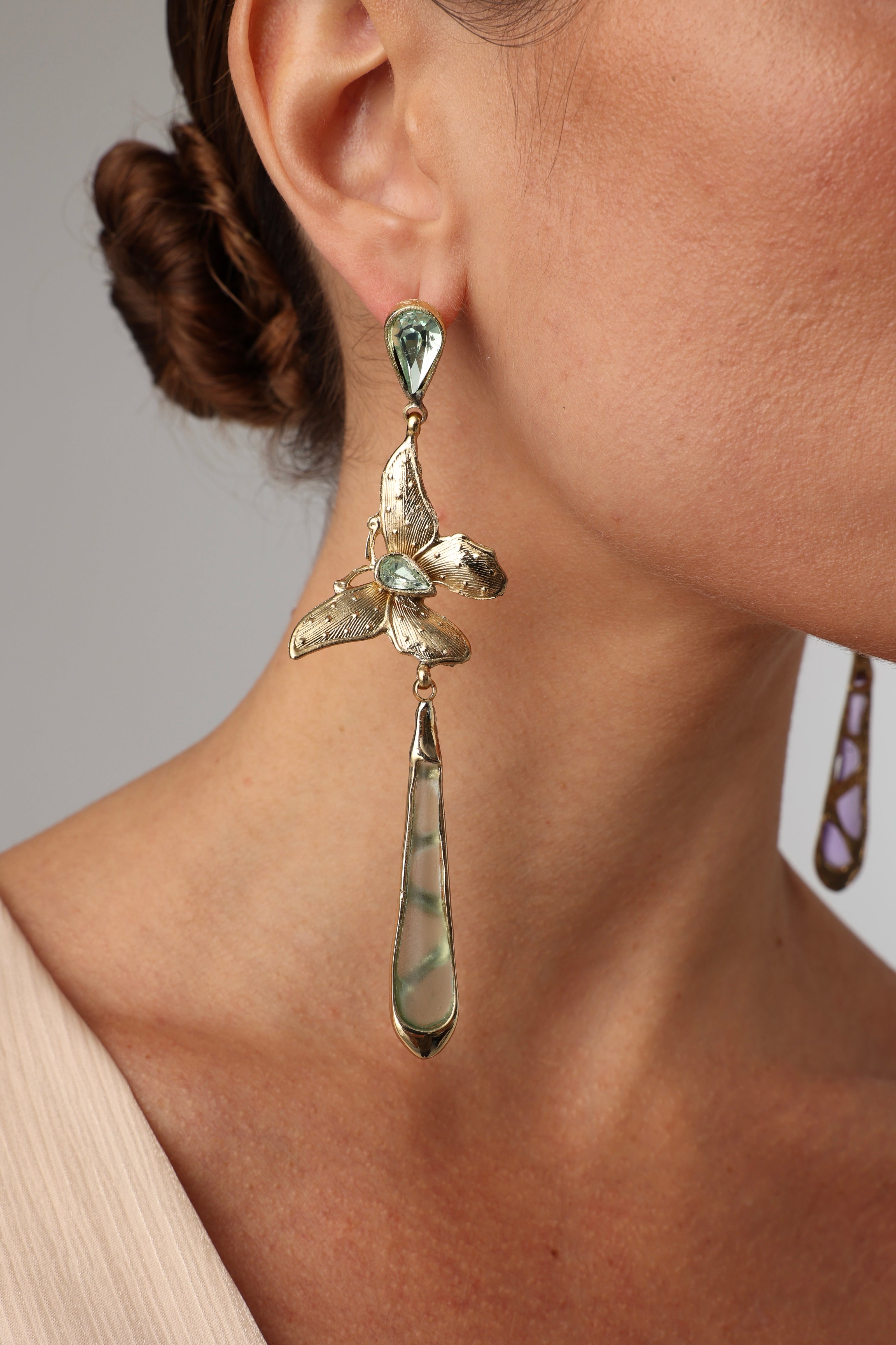 Close-up of a woman wearing bronze butterfly earrings with green crystals and long green drops.