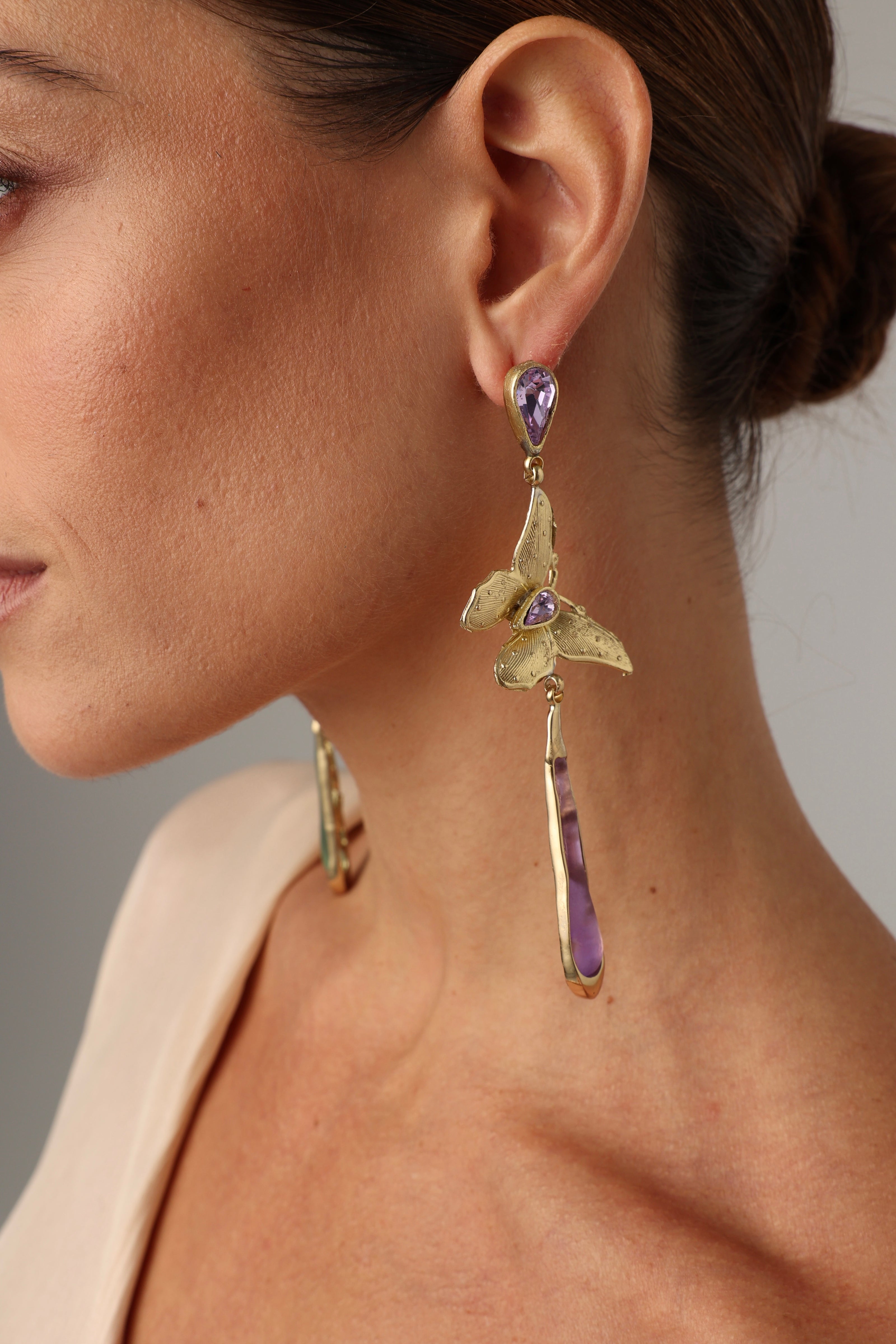 Close-up of a woman wearing bronze butterfly earrings with pink crystals and pearls.