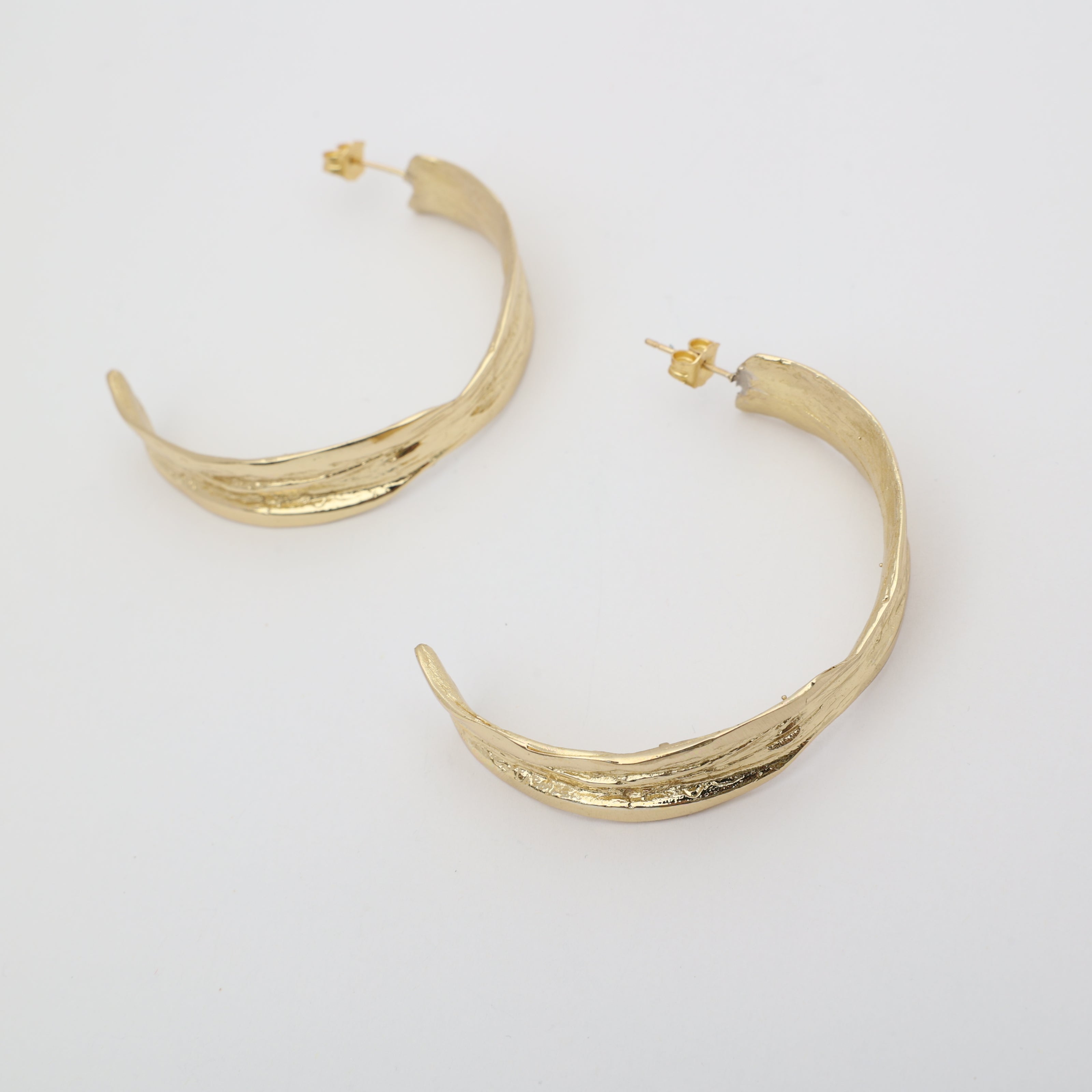 Pair of polished gold leaf-shaped bronze hoop earrings.