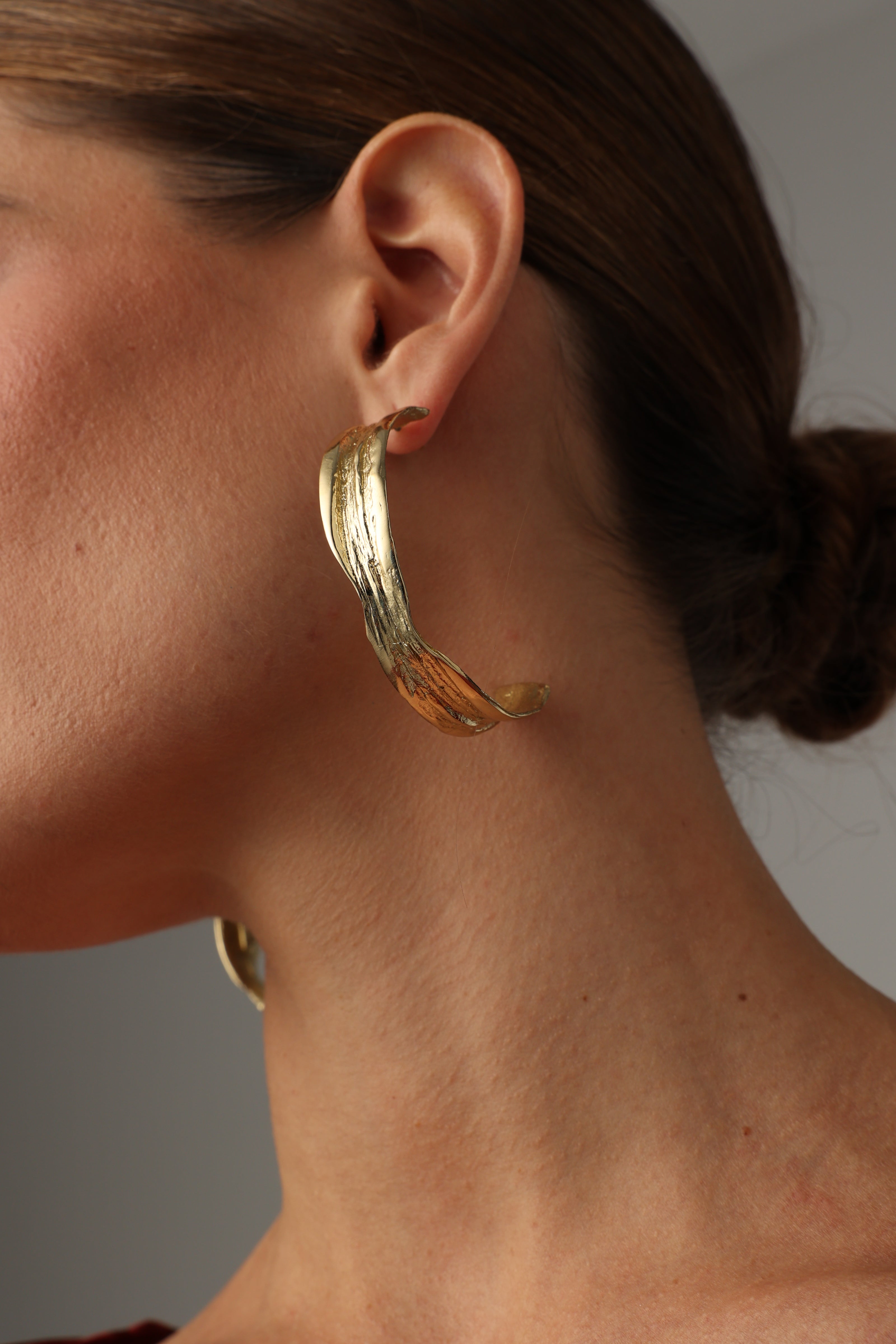 Woman wearing textured, polished gold leaf bronze hoop earrings.