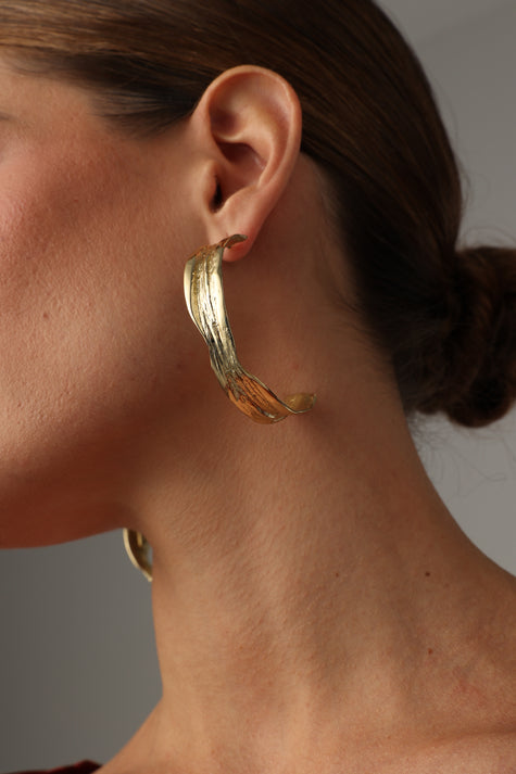 Woman wearing textured, polished gold leaf bronze hoop earrings.