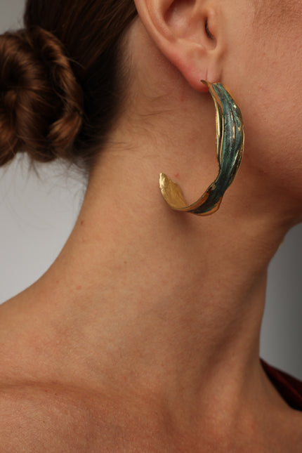 Woman wearing textured bronze hoop earrings with a green patina finish.