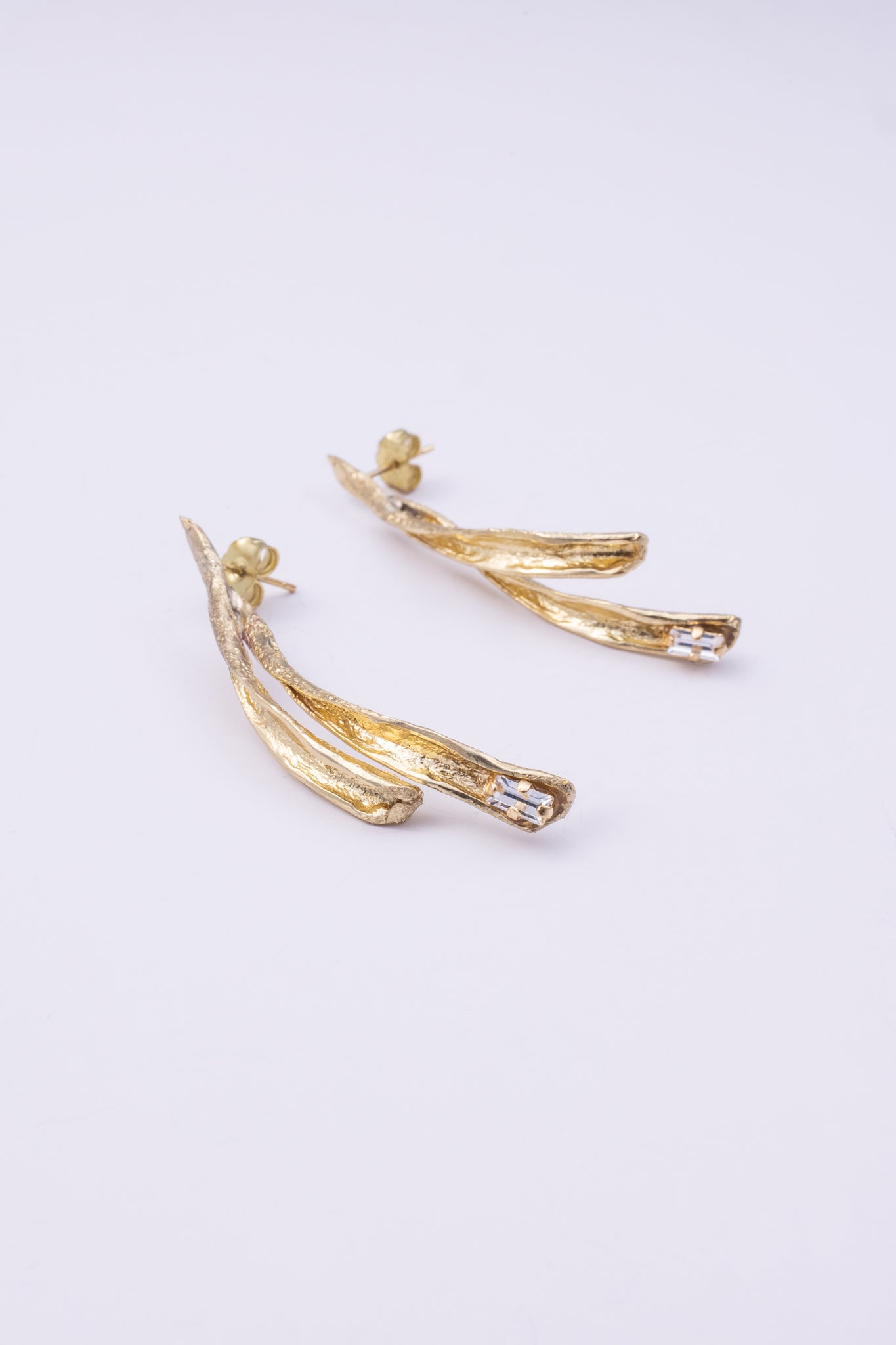 Pixie Earrings flat lay, handmade brass linear earrings with elongated split silhouette and crystal accent