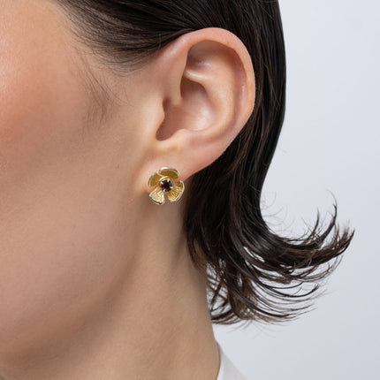 Brass flower stud earring with amethyst crystal center, worn on ear