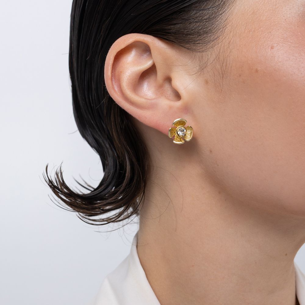Brass flower stud earring with clear crystal center, worn on ear