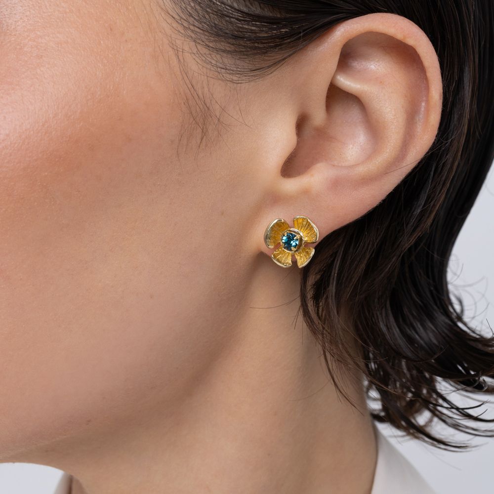 Brass flower stud earring with blue topaz crystal center, worn on ear