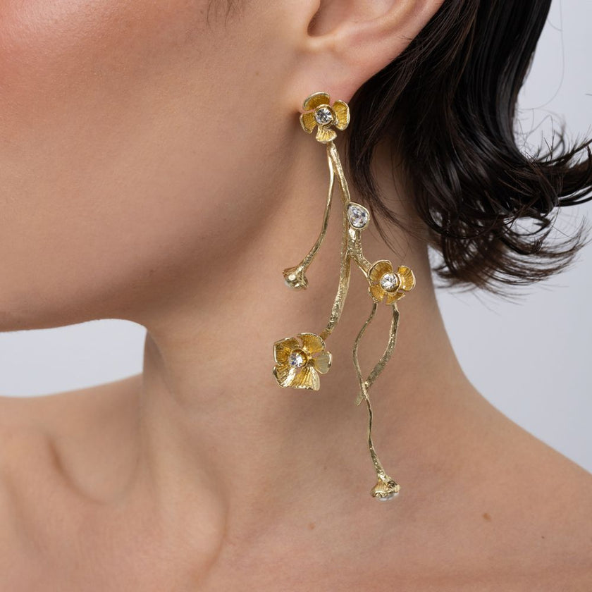 Brass cascading floral drop earring with clear crystal accents, worn on ear