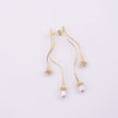 A pair of gold dangle earrings with a textured finish, featuring a small teardrop pearl hanging from each earring, set against a plain light background.
