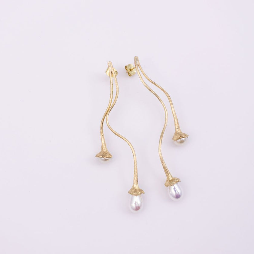 A pair of gold dangle earrings with a textured finish, featuring a small teardrop pearl hanging from each earring, set against a plain light background.