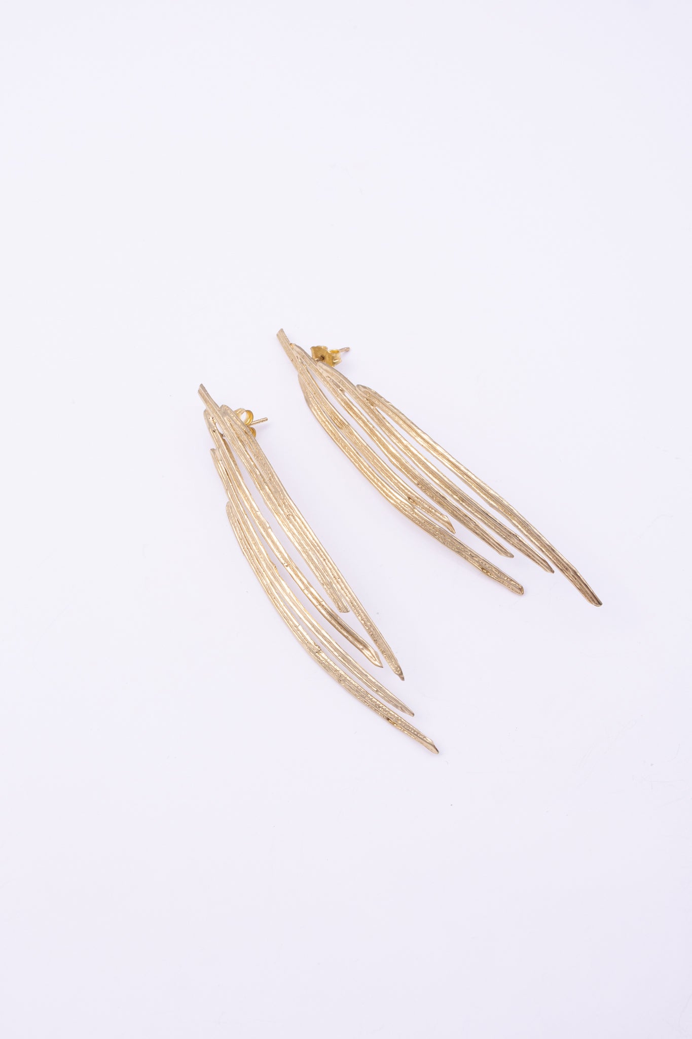 Pine Earrings flat lay, handmade brass linear earrings with elongated peacock feather silhouette