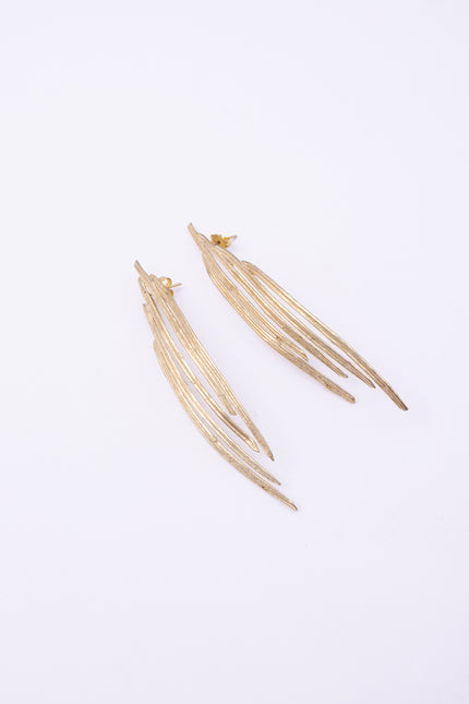 Pine Earrings flat lay, handmade brass linear earrings with elongated peacock feather silhouette