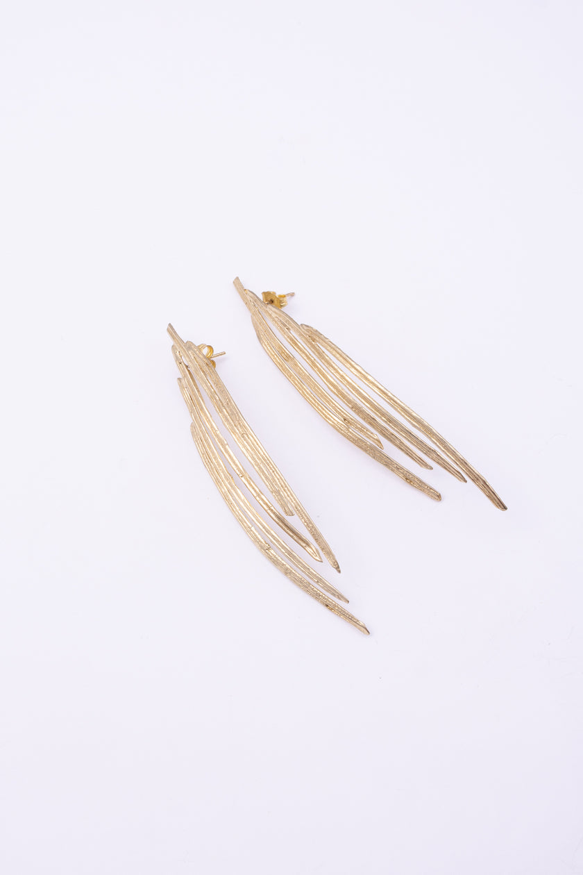 Pine Earrings flat lay, handmade brass linear earrings with elongated peacock feather silhouette