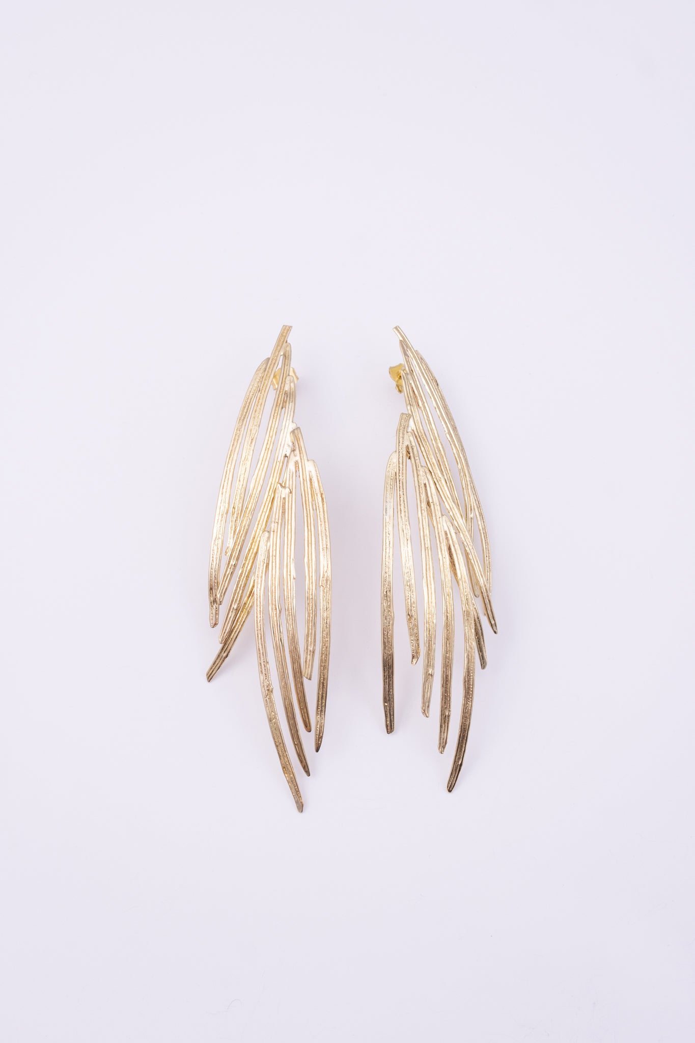 Double Pine Earrings, handmade brass long drop earrings with layered peacock feather blades and etched texture on white background