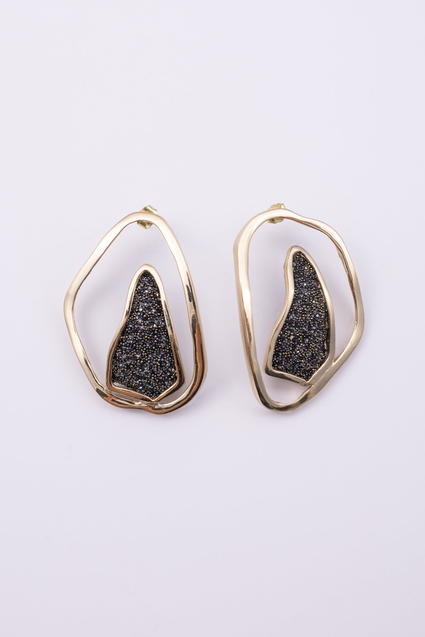 Shimmer Earrings angle view: handmade brass sculptural earrings with overlapping rippled frame